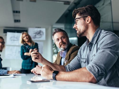 Young designer giving some new ideas about project to his partners in conference room. Business people discussing over new business project in office.